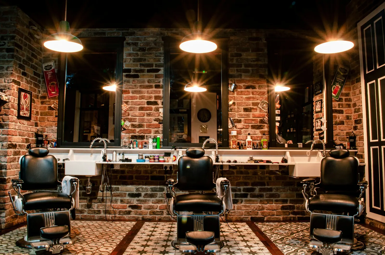 Barbearia com parede de tijolos, cadeiras clássicas e luminárias pendentes