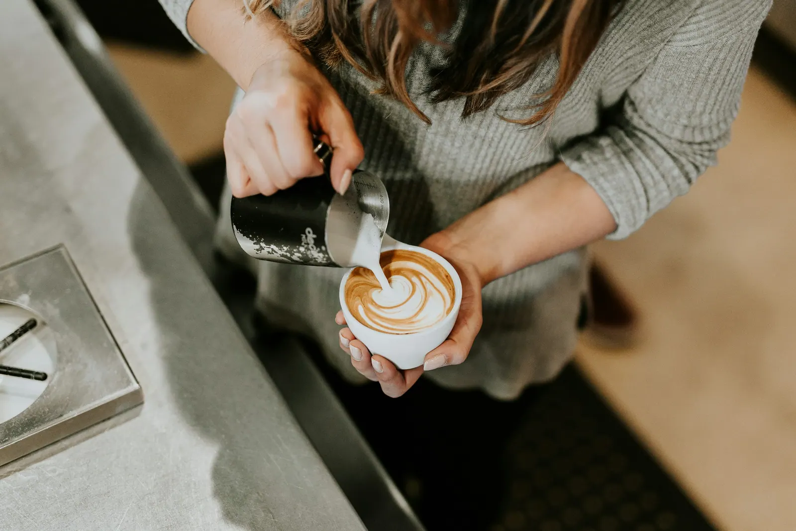 Mãos fazendo latte art em xícara branca