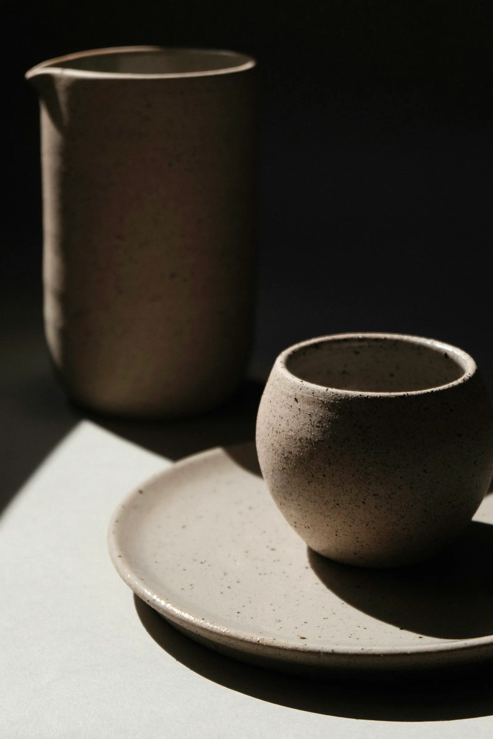 Caneca e pires de cerâmica com sombra marcada sobre fundo escuro