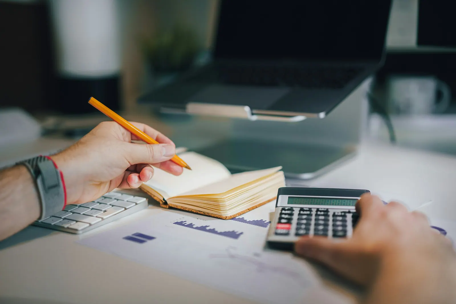 Mão com lápis e calculadora sobre relatórios