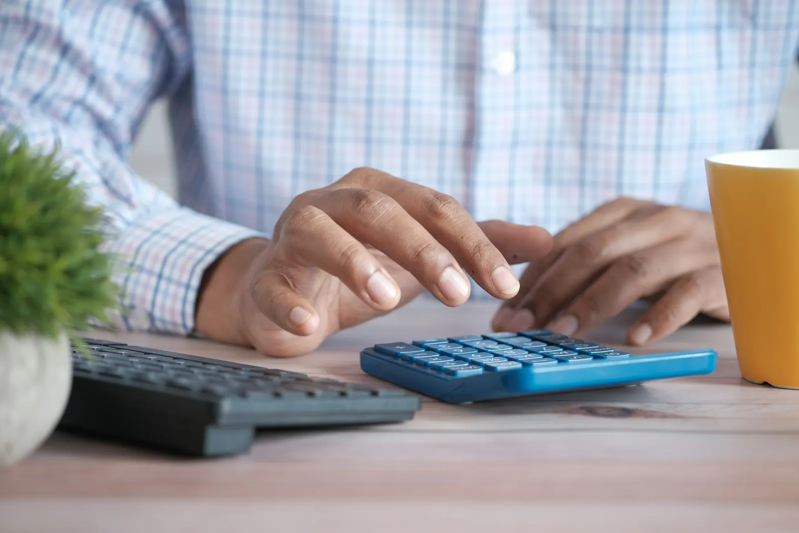 Mãos digitando na calculadora ao lado de uma xícara amarela