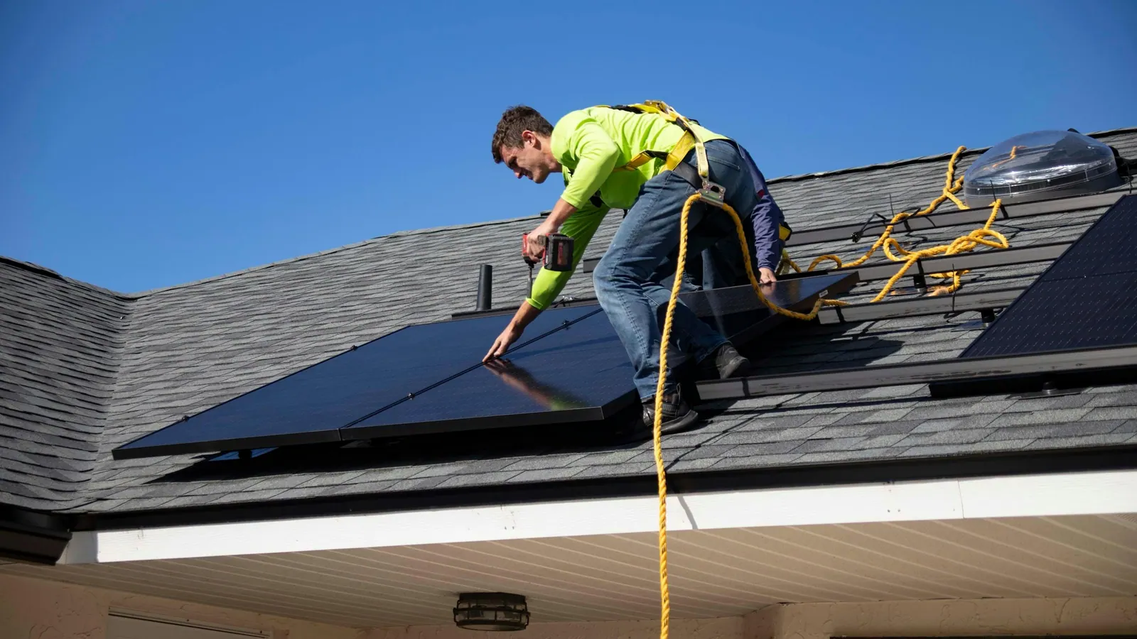 Instalador com cinto de segurança montando painel solar no telhado