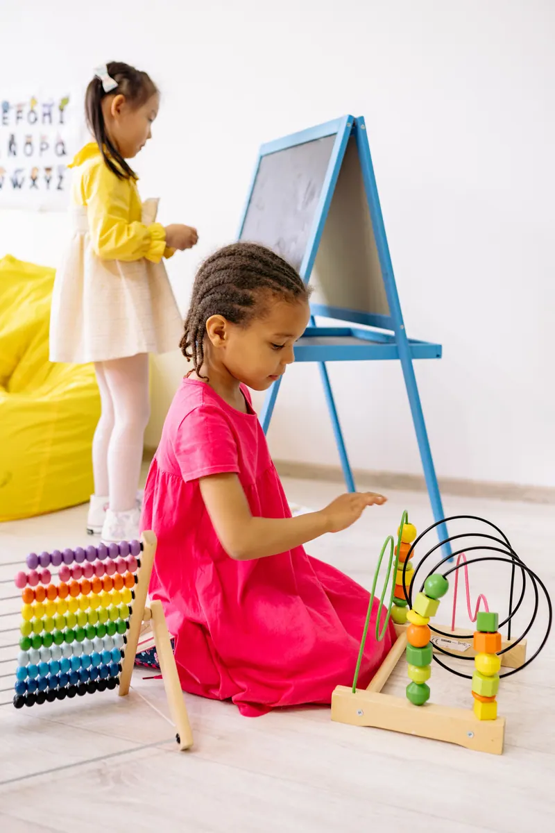 Menina brincando com ábaco colorido ao lado da lousa