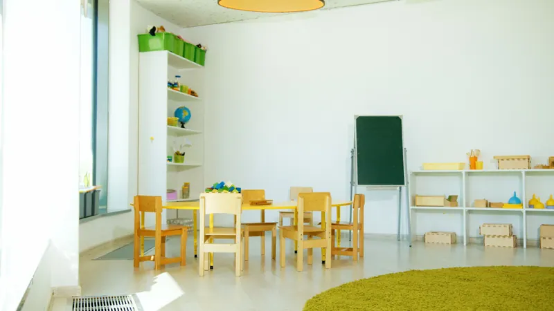 Sala de educação infantil clara com mesinhas e estantes