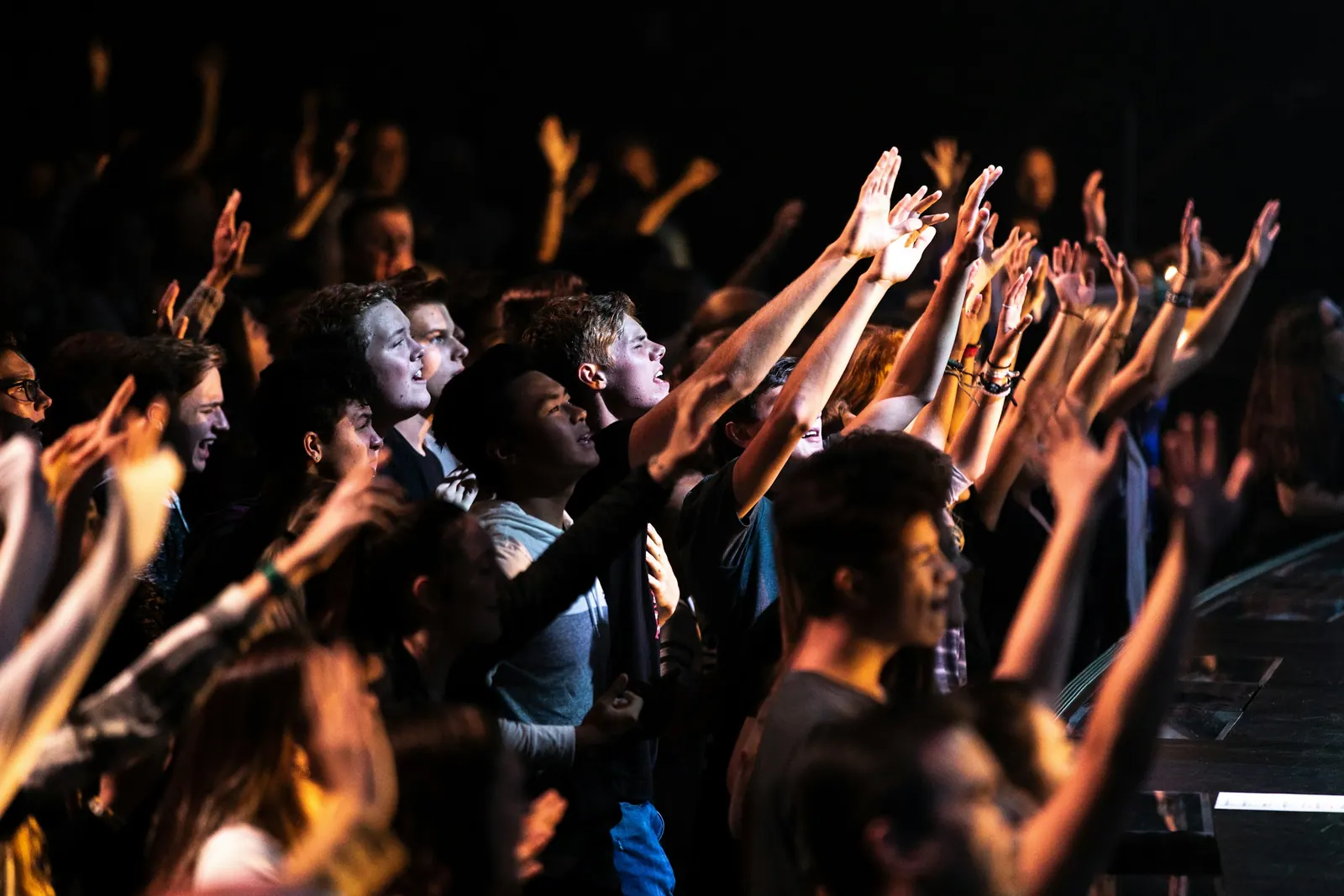 Jovens em louvor com braços erguidos diante do palco