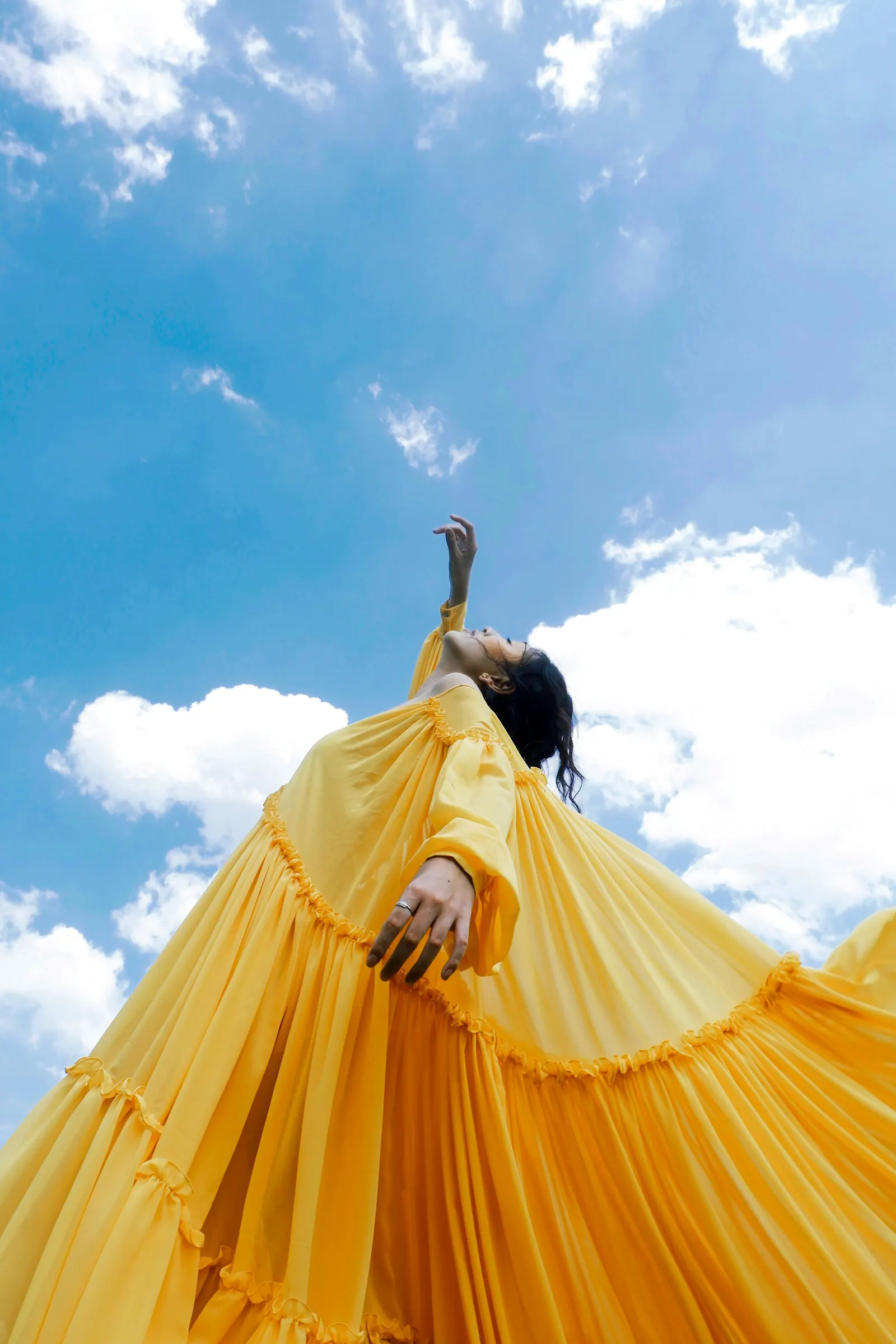 Modelo de vestido amarelo plissado contra o céu azul