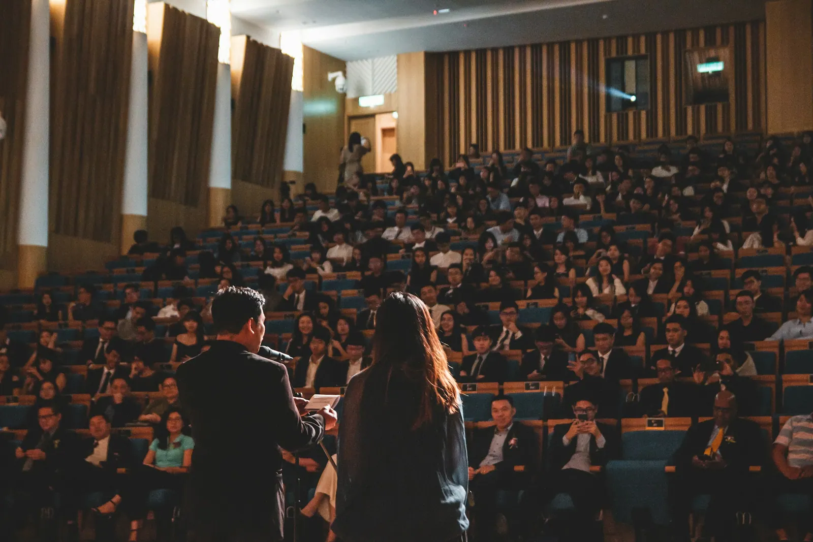 Auditório lotado com palestrantes à frente