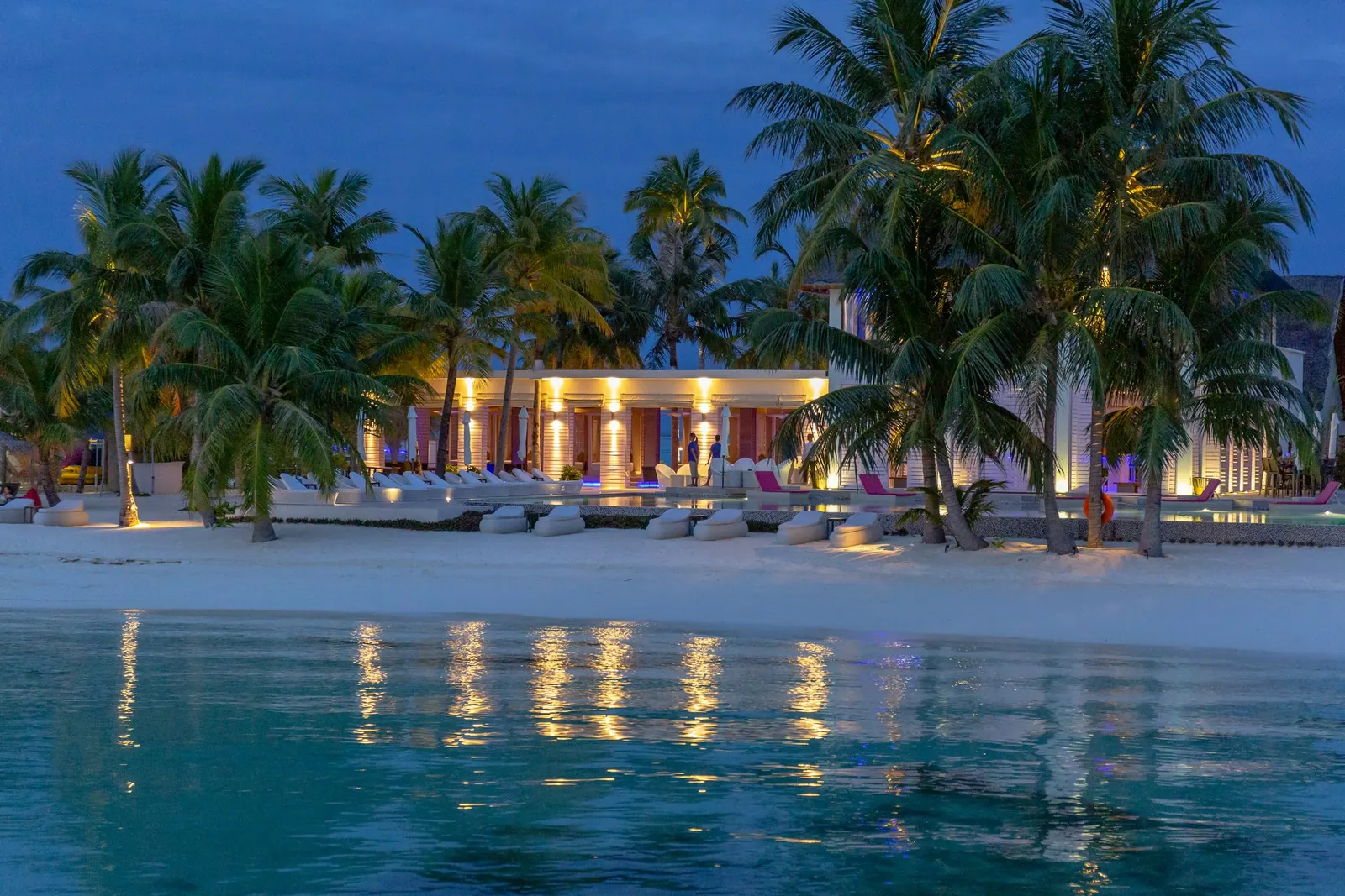 Praia ao anoitecer com luzes refletidas na água