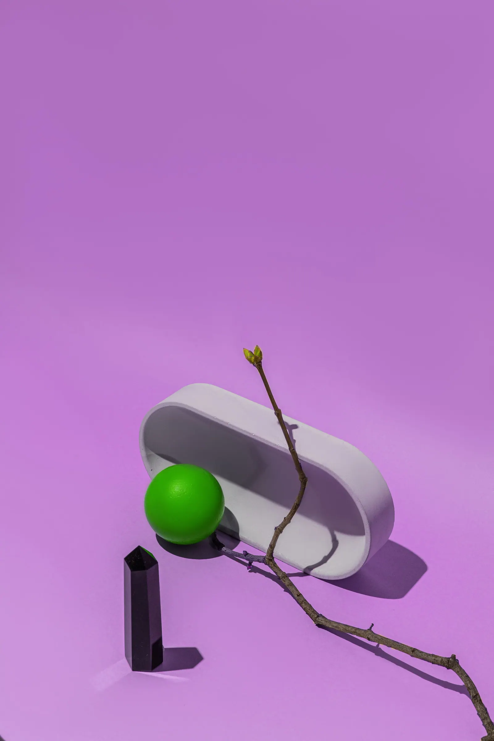 Objetos esculturais com uma esfera verde sobre fundo lilás