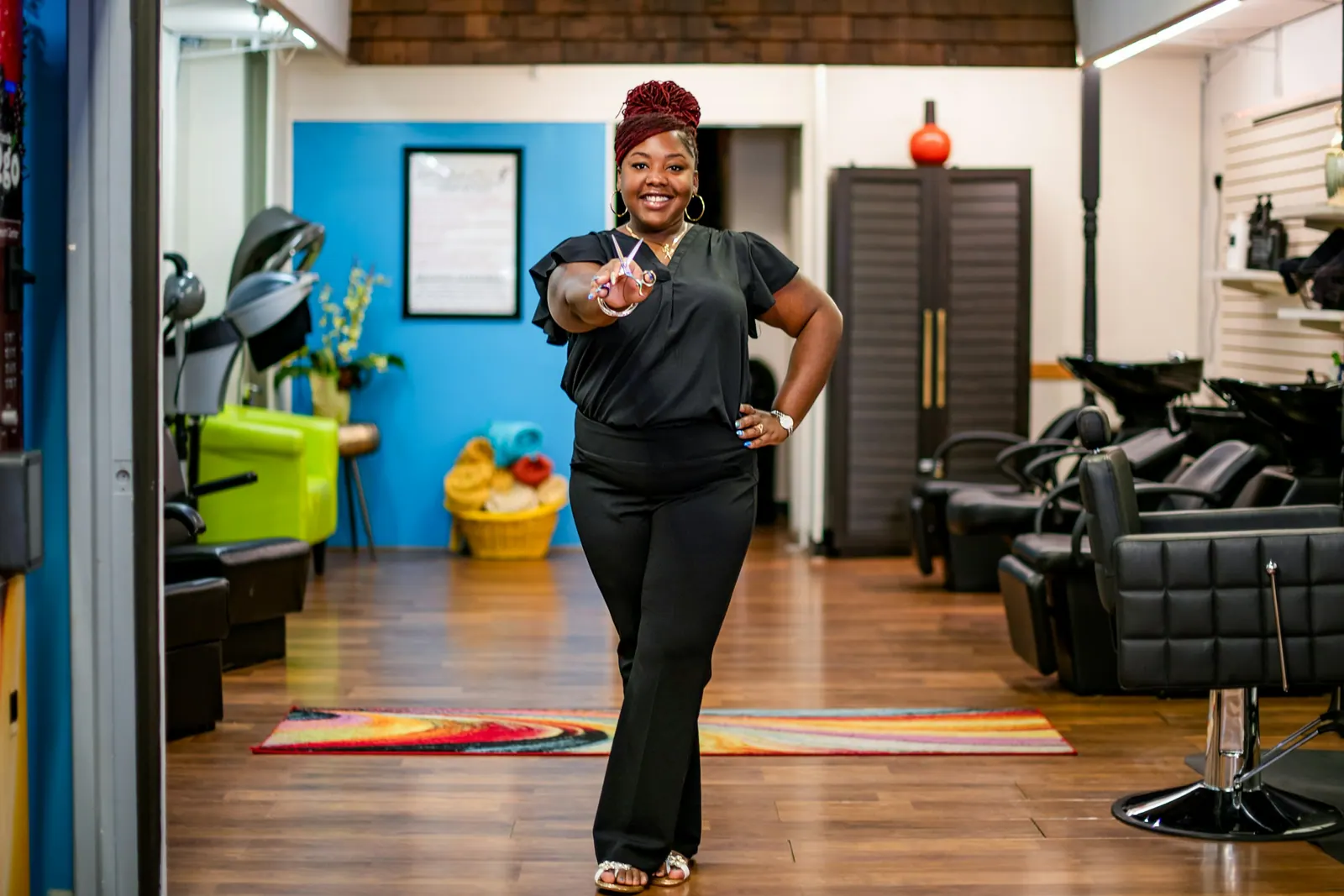 Cabeleireira sorrindo com a tesoura na mão, no salão colorido